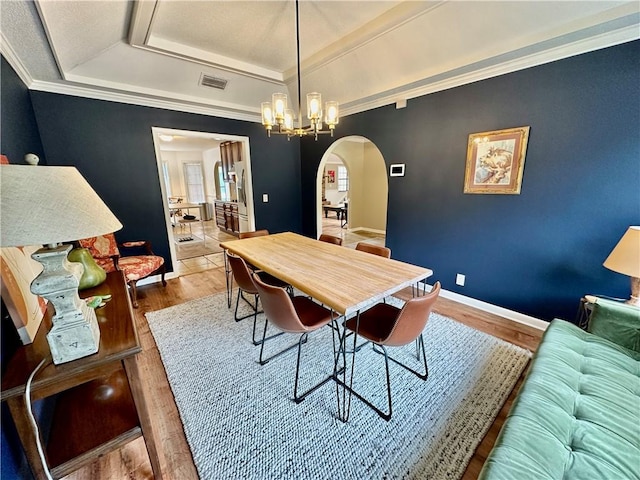 dining area featuring wood finished floors, ornamental molding, visible vents, arched walkways, and a tray ceiling