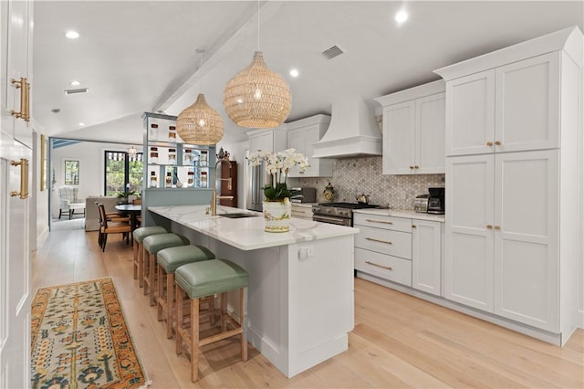 kitchen featuring vaulted ceiling with beams, custom exhaust hood, decorative backsplash, stainless steel range with gas stovetop, and a sink