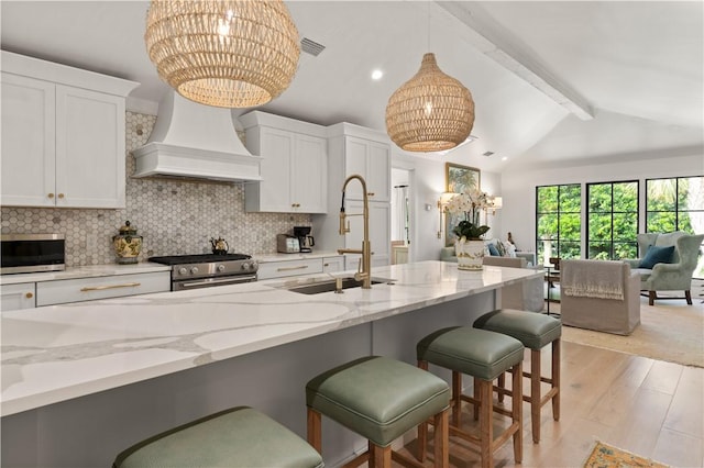 kitchen featuring premium range hood, a sink, open floor plan, appliances with stainless steel finishes, and decorative backsplash