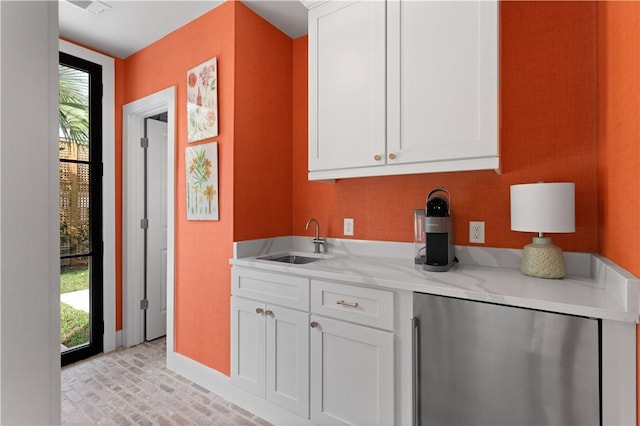 kitchen featuring brick floor, a sink, white cabinetry, fridge, and light stone countertops