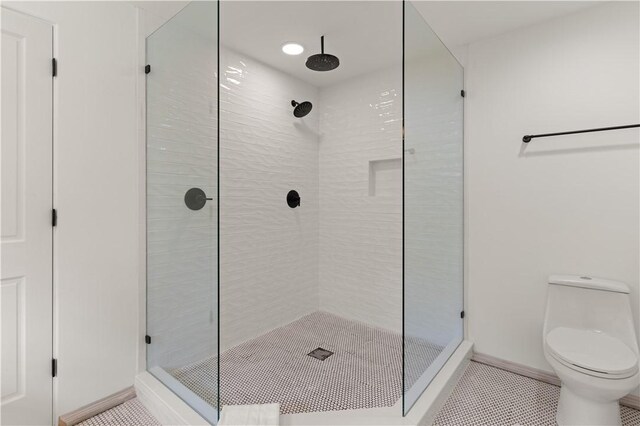 bathroom featuring a stall shower, baseboards, tile patterned flooring, and toilet