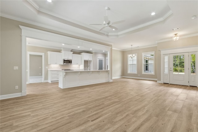 180 Ossabaw Way, Waverly, GA 31565 - unfurnished living room featuring a tray ceiling, ceiling fan, light wood finished floors, ornamental molding, and a chandelier