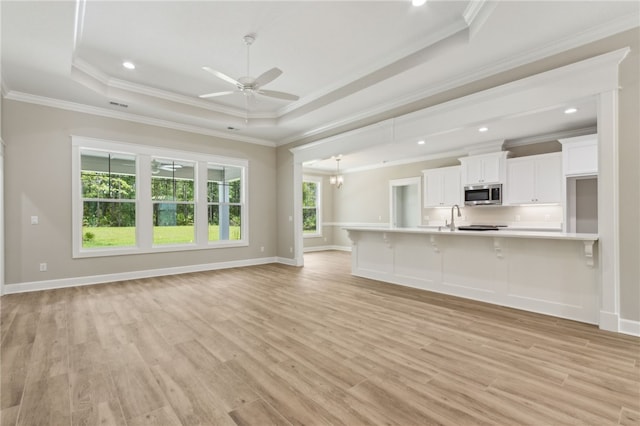 180 Ossabaw Way, Waverly, GA 31565 - unfurnished living room with a tray ceiling, crown molding, light wood-style flooring, a ceiling fan, and a chandelier