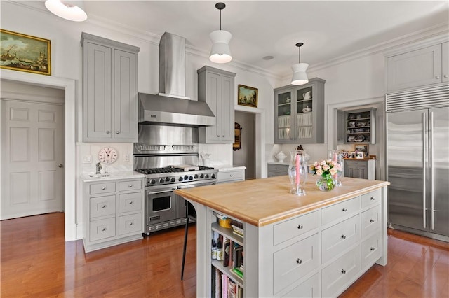 kitchen featuring wall chimney exhaust hood, hanging light fixtures, dark hardwood / wood-style floors, and premium appliances