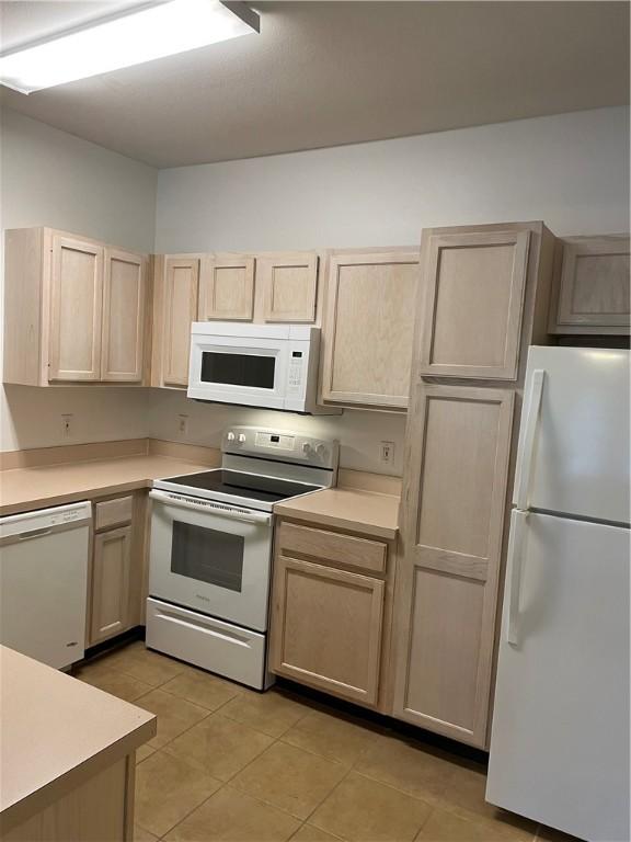 kitchen with light brown cabinetry, light tile patterned floors, and white appliances