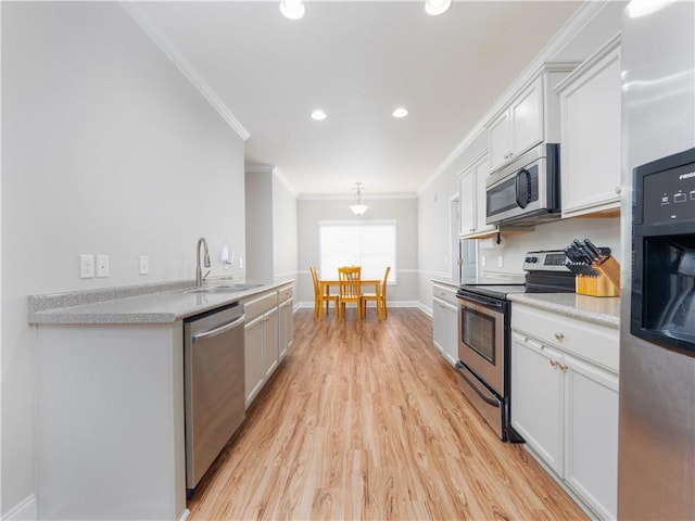 kitchen featuring appliances with stainless steel finishes, white cabinetry, sink, ornamental molding, and light hardwood / wood-style flooring