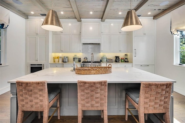 kitchen featuring a spacious island, light stone countertops, beam ceiling, white cabinetry, and a breakfast bar area