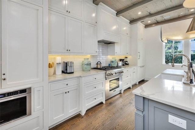 kitchen with sink, stainless steel appliances, light stone counters, hardwood / wood-style floors, and white cabinets