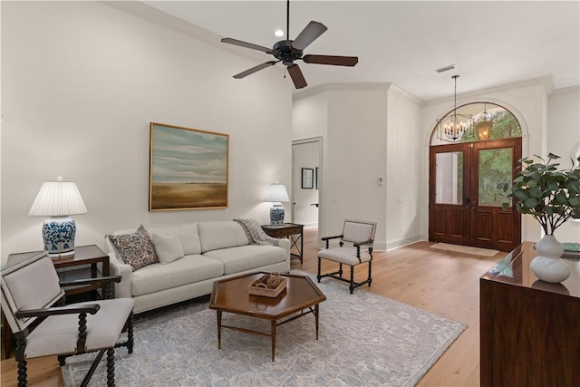 living area featuring ceiling fan with notable chandelier, wood finished floors, visible vents, baseboards, and ornamental molding