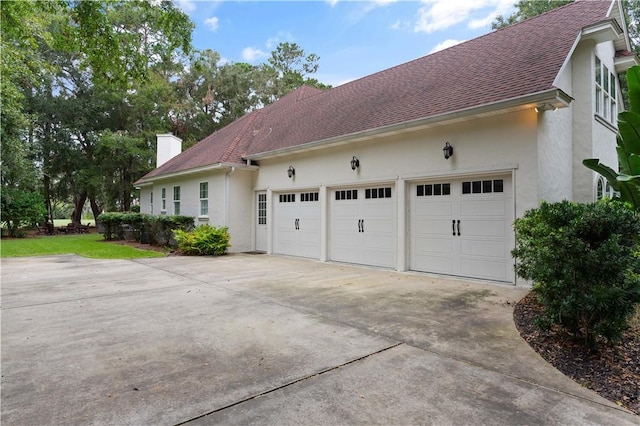 view of side of property with driveway, a shingled roof, a chimney, and stucco siding