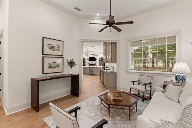 living room with light wood-style floors, baseboards, visible vents, and crown molding