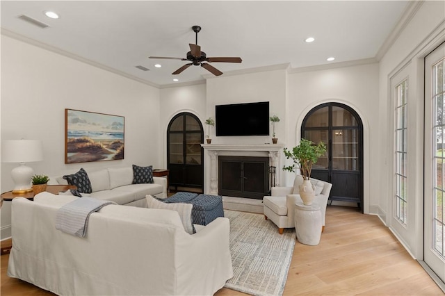 living area featuring recessed lighting, visible vents, light wood-style flooring, ornamental molding, and a glass covered fireplace