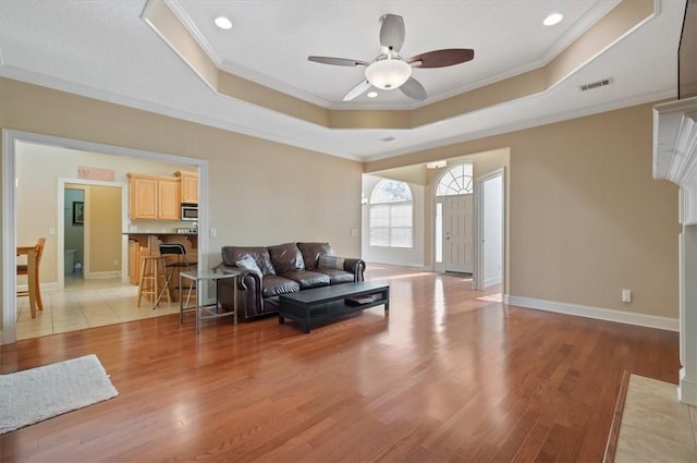 living room featuring ceiling fan, a raised ceiling, light wood-type flooring, and crown molding