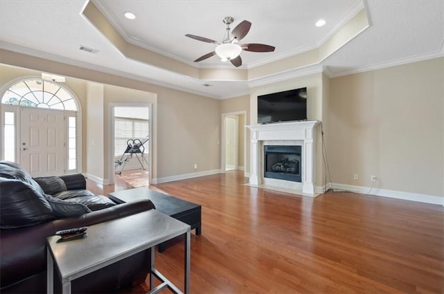 living room with hardwood / wood-style floors, ceiling fan, ornamental molding, and a tray ceiling