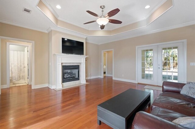 living room featuring ceiling fan, french doors, wood-type flooring, a tray ceiling, and ornamental molding