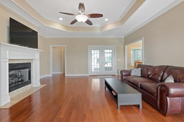 living room featuring crown molding, ceiling fan, light wood-type flooring, a tray ceiling, and a tiled fireplace