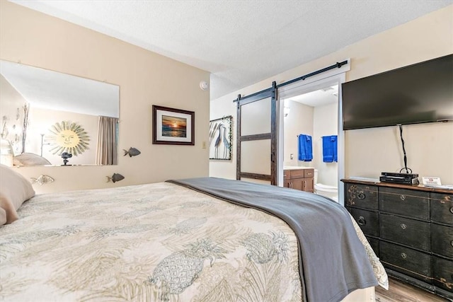 bedroom with ensuite bath, hardwood / wood-style flooring, a textured ceiling, and a barn door