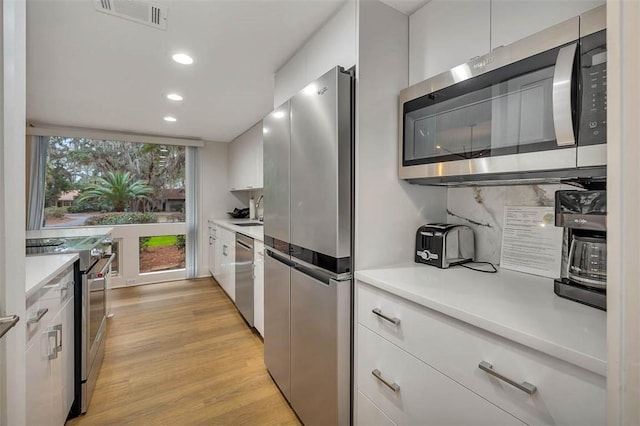 kitchen with sink, light wood-type flooring, appliances with stainless steel finishes, white cabinets, and backsplash