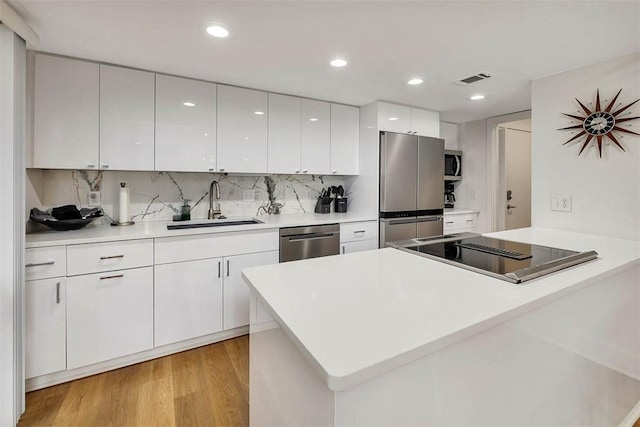 kitchen with sink, white cabinetry, tasteful backsplash, stainless steel appliances, and light hardwood / wood-style floors