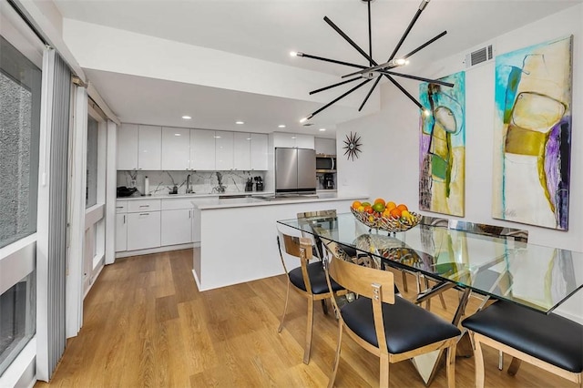 kitchen with a chandelier, light hardwood / wood-style flooring, appliances with stainless steel finishes, decorative backsplash, and white cabinets