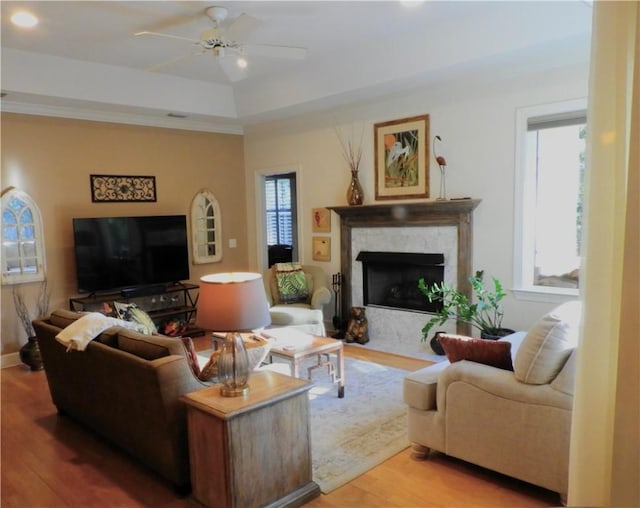 living room with ceiling fan, a raised ceiling, a premium fireplace, and light hardwood / wood-style flooring