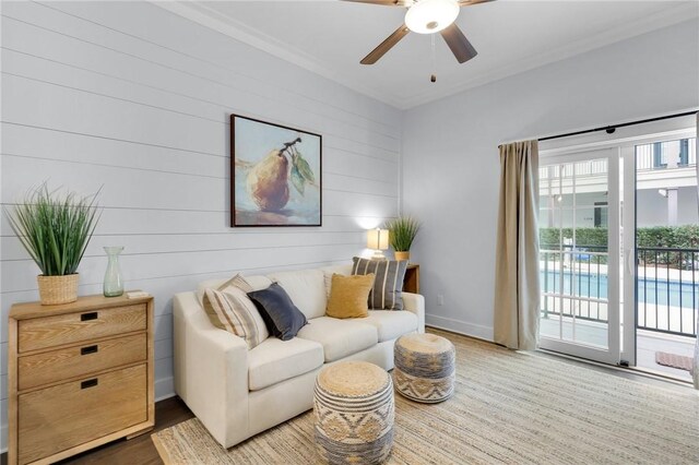 living room featuring ornamental molding, wooden walls, ceiling fan, and dark wood-type flooring