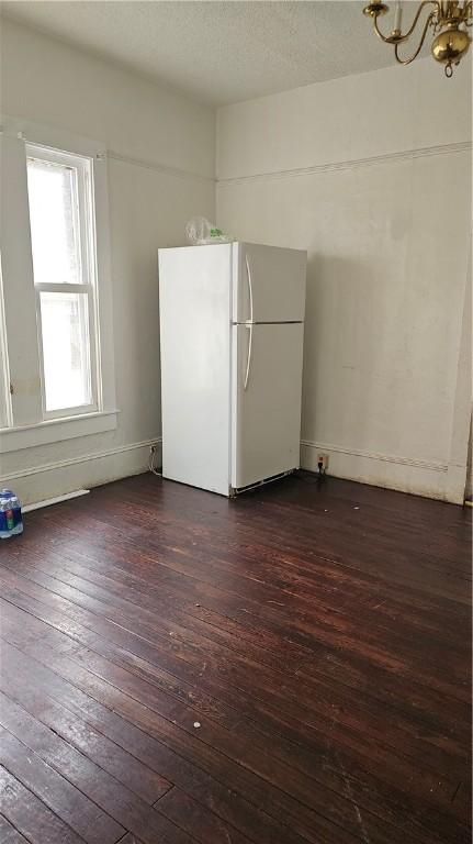 unfurnished room with a textured ceiling, a notable chandelier, and dark wood finished floors
