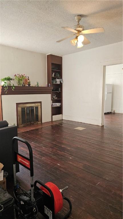 living room featuring a glass covered fireplace, a ceiling fan, a textured ceiling, and wood-type flooring