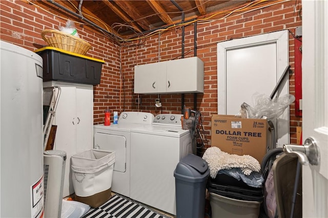 laundry area featuring washing machine and dryer, cabinets, and brick wall