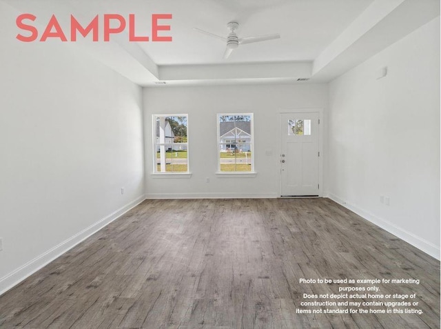 empty room featuring hardwood / wood-style flooring, ceiling fan, and a tray ceiling