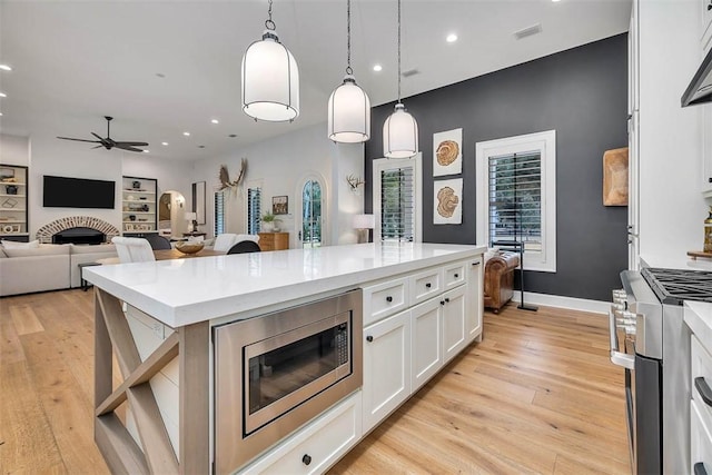 kitchen featuring ceiling fan, light hardwood / wood-style floors, white cabinetry, decorative light fixtures, and stainless steel appliances