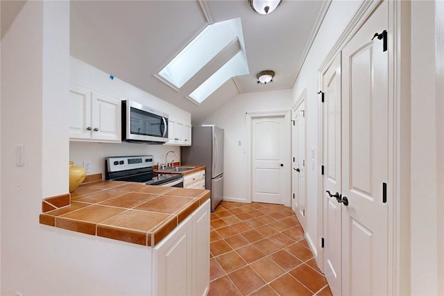 kitchen with sink, appliances with stainless steel finishes, white cabinetry, vaulted ceiling with skylight, and tile countertops