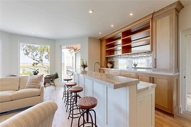 kitchen featuring a kitchen bar, a kitchen island with sink, light brown cabinetry, and light hardwood / wood-style floors