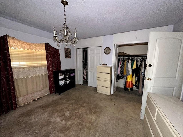 unfurnished bedroom featuring an inviting chandelier, two closets, carpet, and a textured ceiling