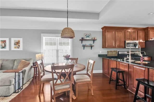 kitchen featuring dark wood finished floors, stainless steel microwave, brown cabinets, stove, and hanging light fixtures