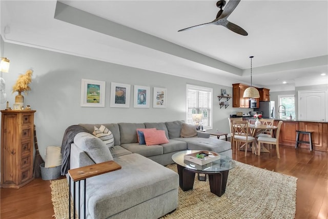 living room featuring dark wood-style floors, plenty of natural light, a raised ceiling, and ceiling fan