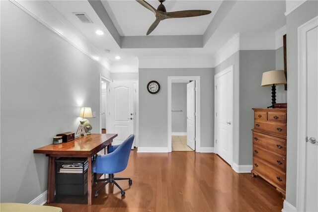 office space with baseboards, visible vents, a raised ceiling, and wood finished floors