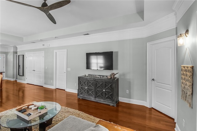 living room with dark wood-style floors, a tray ceiling, a ceiling fan, and baseboards