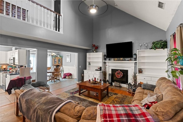 living room with light hardwood / wood-style floors, high vaulted ceiling, and an inviting chandelier