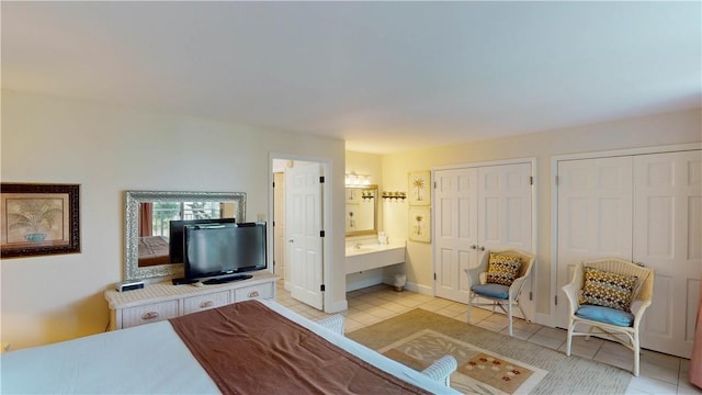 tiled bedroom featuring multiple closets and ensuite bathroom