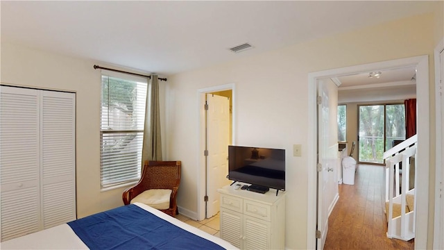 bedroom featuring a closet, light wood-type flooring, crown molding, and multiple windows