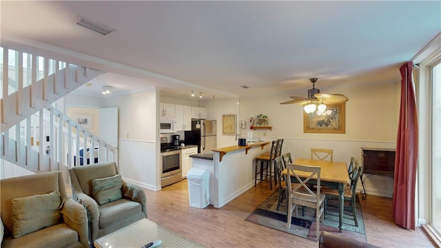 interior space featuring kitchen peninsula, stainless steel appliances, ceiling fan, crown molding, and white cabinets