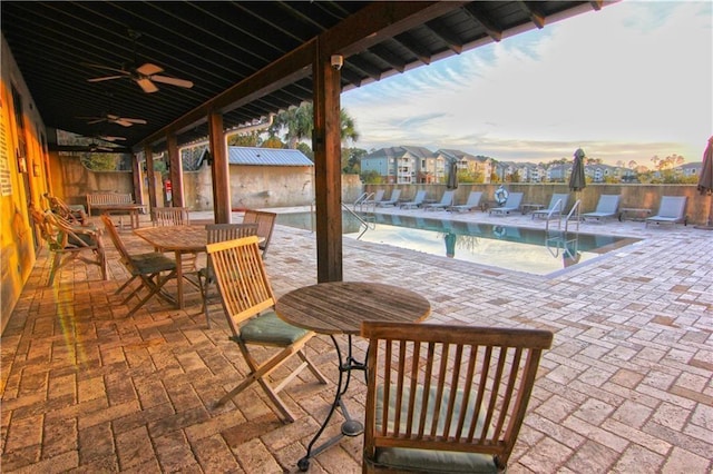 patio terrace at dusk featuring ceiling fan and a community pool