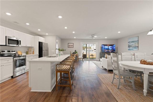 kitchen with appliances with stainless steel finishes, dark hardwood / wood-style flooring, white cabinetry, and a kitchen island with sink