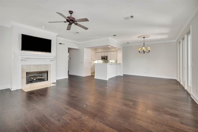unfurnished living room featuring crown molding, dark wood-style flooring, baseboards, a tile fireplace, and ceiling fan with notable chandelier