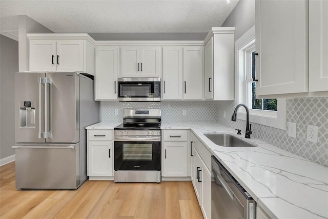 kitchen featuring appliances with stainless steel finishes, light stone counters, sink, light hardwood / wood-style floors, and white cabinetry