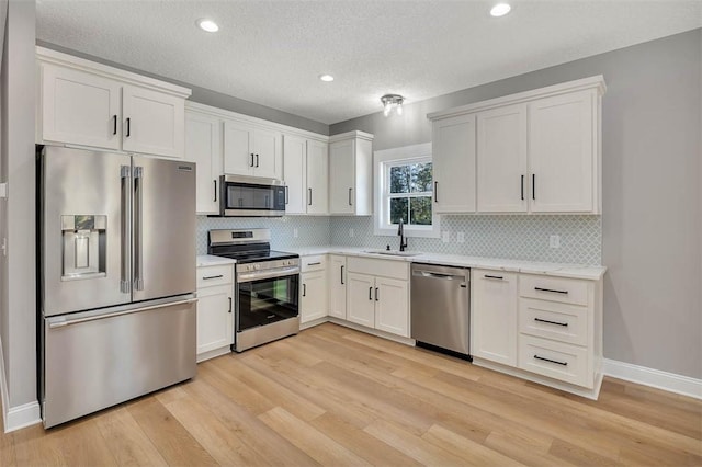 kitchen with white cabinetry, sink, stainless steel appliances, light hardwood / wood-style flooring, and a textured ceiling