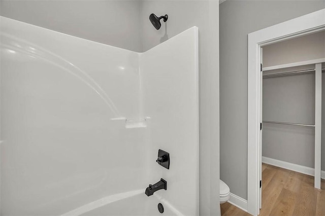 bathroom with wood-type flooring,  shower combination, and toilet