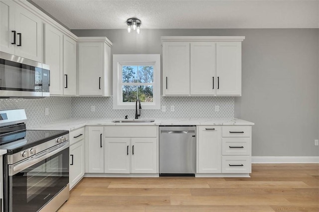 kitchen featuring light wood-type flooring, backsplash, stainless steel appliances, sink, and white cabinets