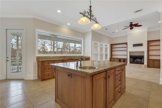 kitchen with sink, light tile patterned floors, a fireplace, an island with sink, and decorative light fixtures